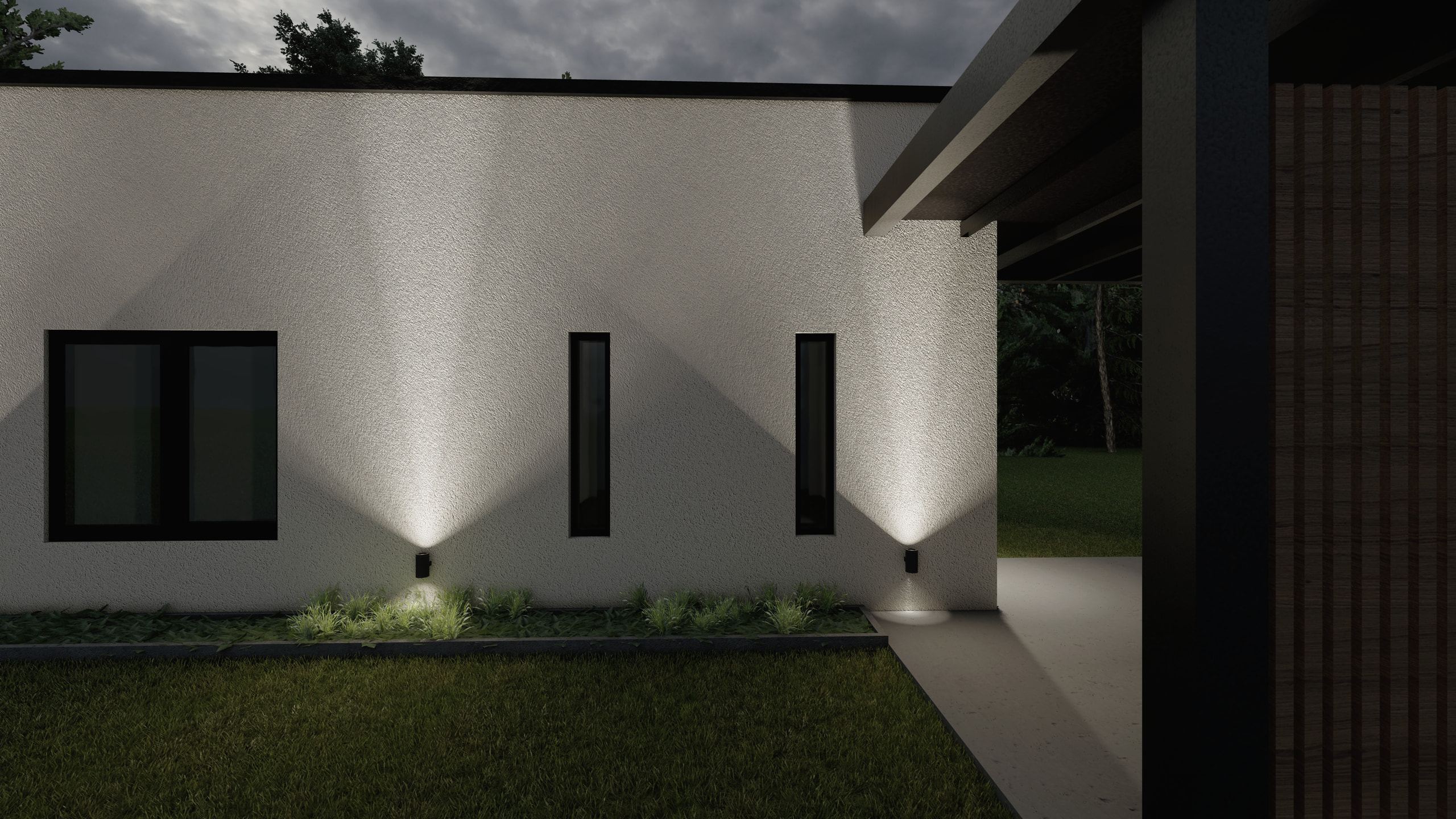 The white wall at night: narrow windows, raking light from wall washers and, on the right, the edge of the timber pergola.