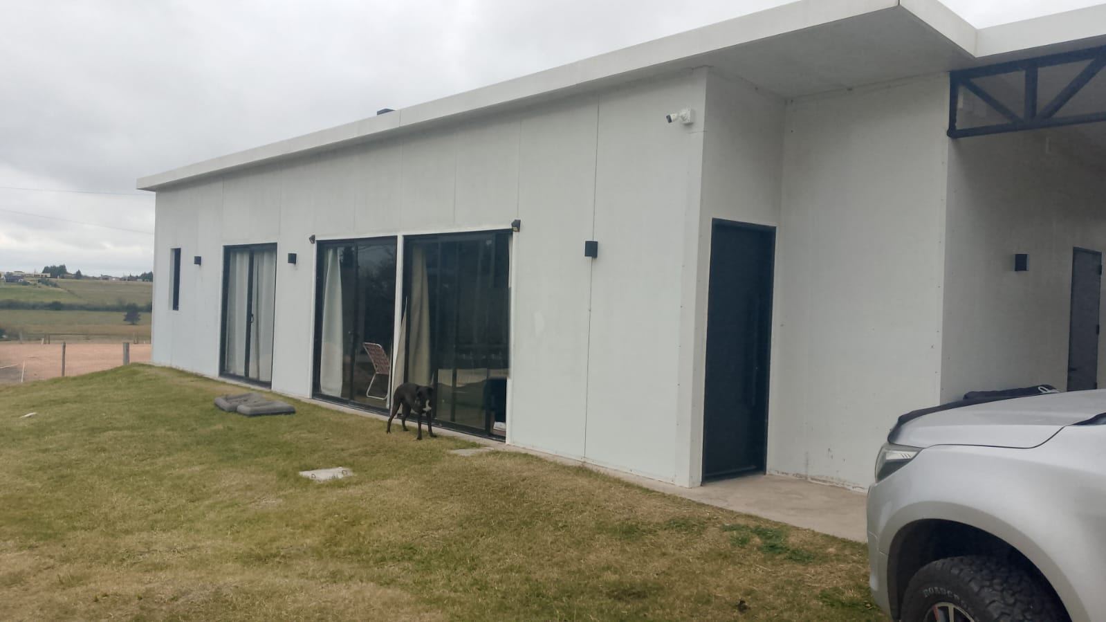 Foto de la casa antes de la propuesta: muros blancos sin terminación, carpinterías negras y césped.